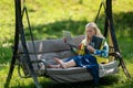 Senior woman with laptop and documents working in garden on rocking couch, green home office concept