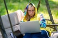 Senior woman with laptop and documents working in garden on rocking couch, green home office concept