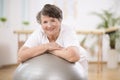 Senior woman leaning on grey gymnastic ball at physiotherapy center