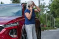 Woman leans against her red car and calls for help after causing an accident