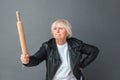 Senior woman in leather jacket studio standing isolated on gray with rolling pin threatening someone angry Royalty Free Stock Photo