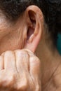 Senior woman left hand pulling down her left ear, Grey curly hairs, Swimming pool background, Close up, Symptom of hearing loss