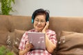 Senior woman is listen music via computer tablet on sofa at home. Royalty Free Stock Photo