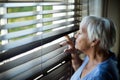 Senior woman looking out from window blind