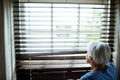 Senior woman looking out from window blind