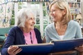 Senior Woman Looks At Photo Album With Mature Female Neighbor