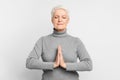 Senior woman in a meditation pose on grey background