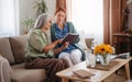 Senior woman and nurse reading book together, having nice time in home. Royalty Free Stock Photo