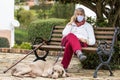 Senior woman outdoors using her cell phone wearing a home made face mask during the coronavirus quarantine de-escalation