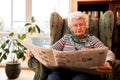 Senior woman in pansion relaxing at home while reading a newspaper