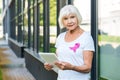 senior woman with pink ribbon on t-shirt using digital tablet and looking at camera breast cancer awareness concept Royalty Free Stock Photo