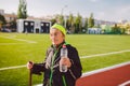 Senior woman practicing nordic walking at city stadium and stopped to quench thirst, drink water from bottle. Age, maturity, Royalty Free Stock Photo