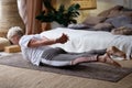 Senior woman practicing yoga at home indoor, doing Salabhasana or Locust pose