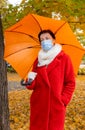 Senior woman protective medical mask autumn park age middle 50 plus umbrella red orange Royalty Free Stock Photo