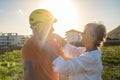 Senior woman puts protective helmet on her husband to ride a bicycle. Bright sunset light