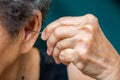 Senior woman putting earpick into her left ear, Grey curly hairs, Swimming pool background, Healthcare, Symptom of hearing loss