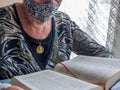 Senior woman reading bible with gold medallion of virgin mary