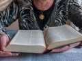 Senior woman reading bible with gold medallion of virgin mary Royalty Free Stock Photo