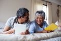 Senior woman reading a book and senior man using digital tablet on bed Royalty Free Stock Photo
