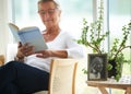 Senior, woman and relaxing with book in home for reading, wellness or self care. Elderly person, glasses and smile with