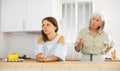 Senior woman scolding her adult daughter cooking breakfast in modern kitchen Royalty Free Stock Photo