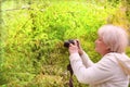 Senior woman shooting photo by digital camera. Shooting blooming bird cherry tree. Concept of aged people and photography. Cloudy Royalty Free Stock Photo