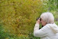 Senior woman shooting photo by digital camera. Shooting blooming bird cherry tree. Concept of aged people and photography. Cloudy Royalty Free Stock Photo