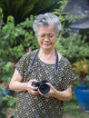 Senior woman with short gray hair wearing glasses and shooting photography by a digital camera at the garden Royalty Free Stock Photo