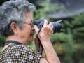 Senior woman with short gray hair wearing glasses and shooting photography by a digital camera at the park. Concept of aged people Royalty Free Stock Photo