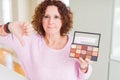 Senior woman showing nudes eyeshadows colors with angry face, negative sign showing dislike with thumbs down, rejection concept