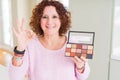 Senior woman showing nudes eyeshadows colors doing ok sign with fingers, excellent symbol Royalty Free Stock Photo
