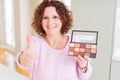 Senior woman showing nudes eyeshadows colors happy with big smile doing ok sign, thumb up with fingers, excellent sign