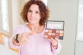 Senior woman showing nudes eyeshadows colors pointing with finger to the camera and to you, hand sign, positive and confident