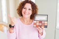 Senior woman showing nudes eyeshadows colors pointing and showing with thumb up to the side with happy face smiling