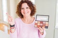 Senior woman showing nudes eyeshadows colors very happy pointing with hand and finger to the side