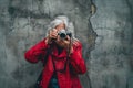 Senior woman with silver hair in red jacket captures the world with camera