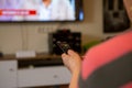 A senior woman sits in front of the television watching television. She holds a remote control in her hand that she points at the