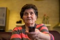 A senior woman sits in front of the television watching television. She holds a remote control in her hand that she points at the Royalty Free Stock Photo