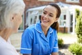 Senior Woman Sitting On Bench And Talking With Nurse In Retirement Home