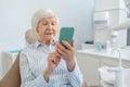 Senior woman sitting at the dentists office and using her smartphone Royalty Free Stock Photo