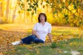 Senior woman is sitting on the grass with yellow leaves in autumn Royalty Free Stock Photo