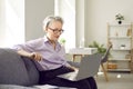 Senior woman sitting with laptop on couch at home and having video call or watching webinar Royalty Free Stock Photo