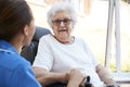 Senior Woman Sitting In Motorized Wheelchair Talking With Nurse In Retirement Home