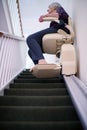 Senior Woman Sitting On Stair Lift At Home To Help Mobility