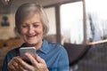 Senior woman with smartphone at home sitting at the window Royalty Free Stock Photo