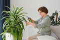 Senior woman sprays plants in flowerpots. Happy female caring for house plant. Mature Woman taking care of plants at her Royalty Free Stock Photo