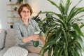 Senior woman sprays plants in flowerpots. Happy female caring for house plant. Mature Woman taking care of plants at her Royalty Free Stock Photo