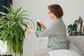 Senior woman sprays plants in flowerpots. Happy female caring for house plant. Mature Woman taking care of plants at her Royalty Free Stock Photo