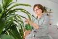 Senior woman sprays plants in flowerpots. Happy female caring for house plant. Mature Woman taking care of plants at her Royalty Free Stock Photo