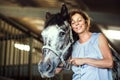 A senior woman standing close to a horse in a stable, holding it. Royalty Free Stock Photo